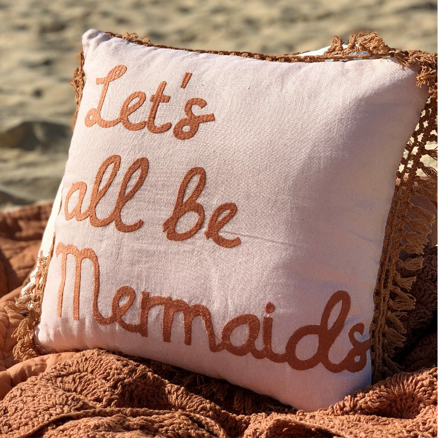 Decorative pillow with 'Let's all be mermaids' text on a textured surface.