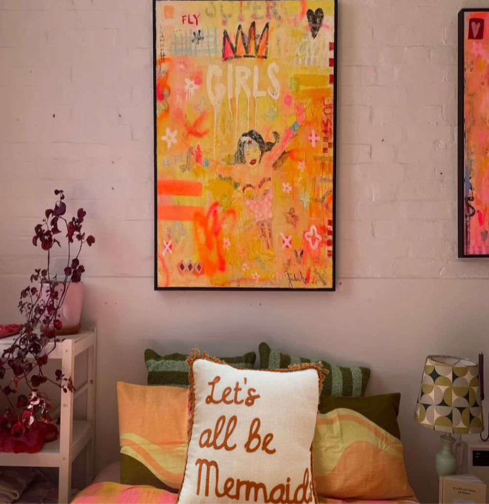 Decorative pillow with 'Let's all be Mermaids' text in a room with colorful wall art.