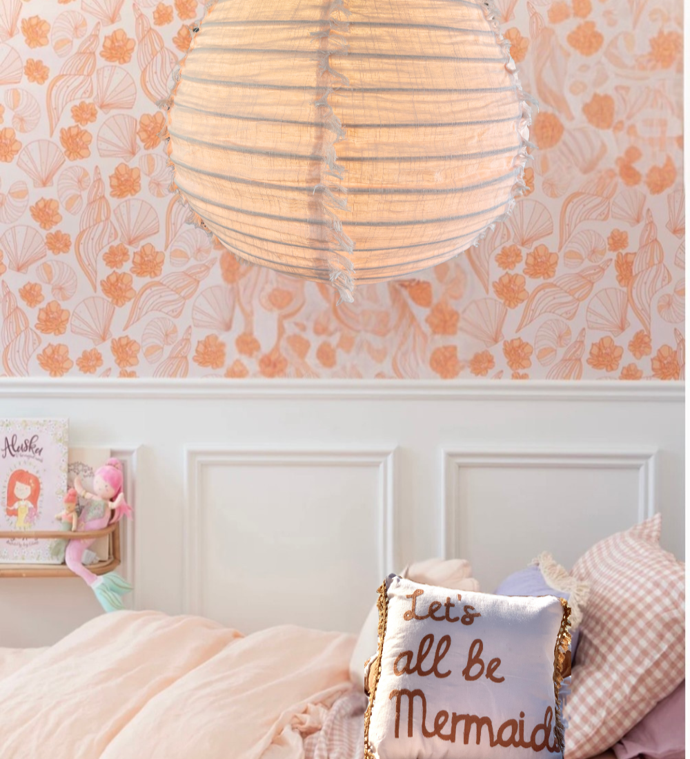 A blush pink linen light shade with a fringed edge is placed above a bed in a little girl's room.
