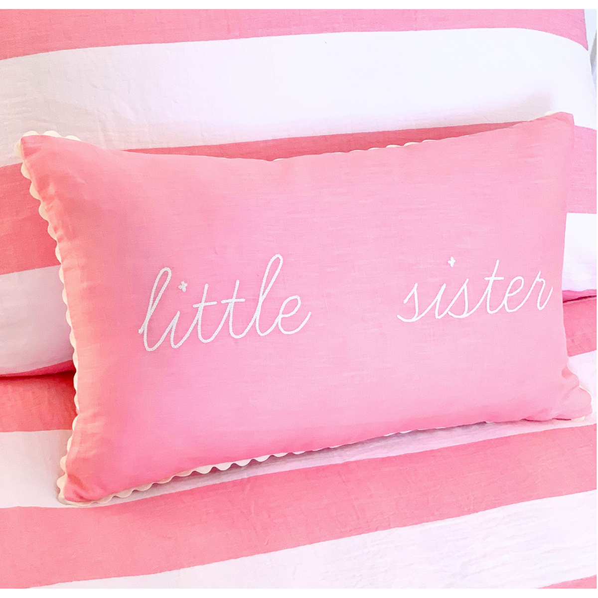 Pink pillow with 'little sister' text on a striped background
