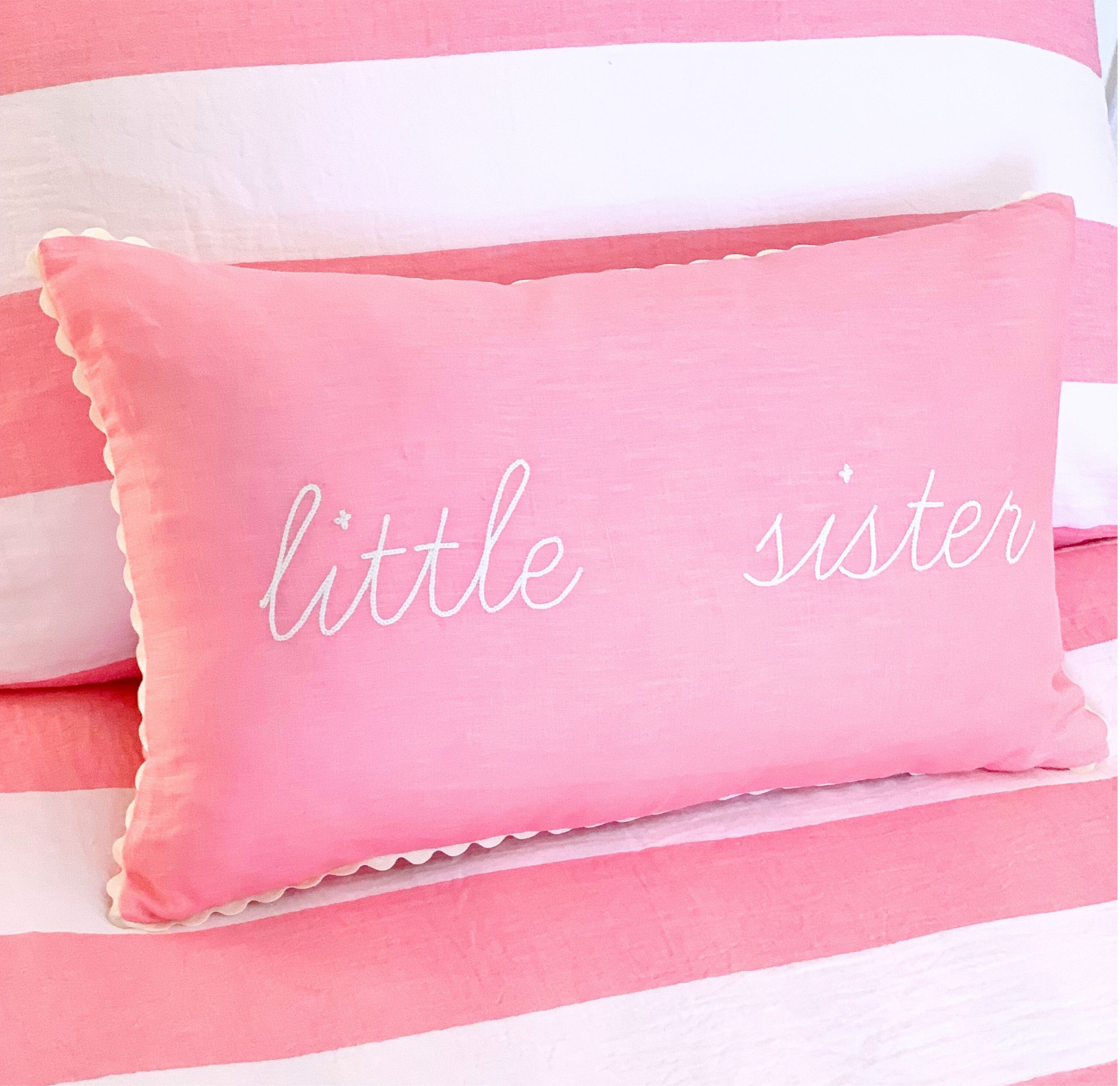 Pink pillow with 'little sister' text on a striped background