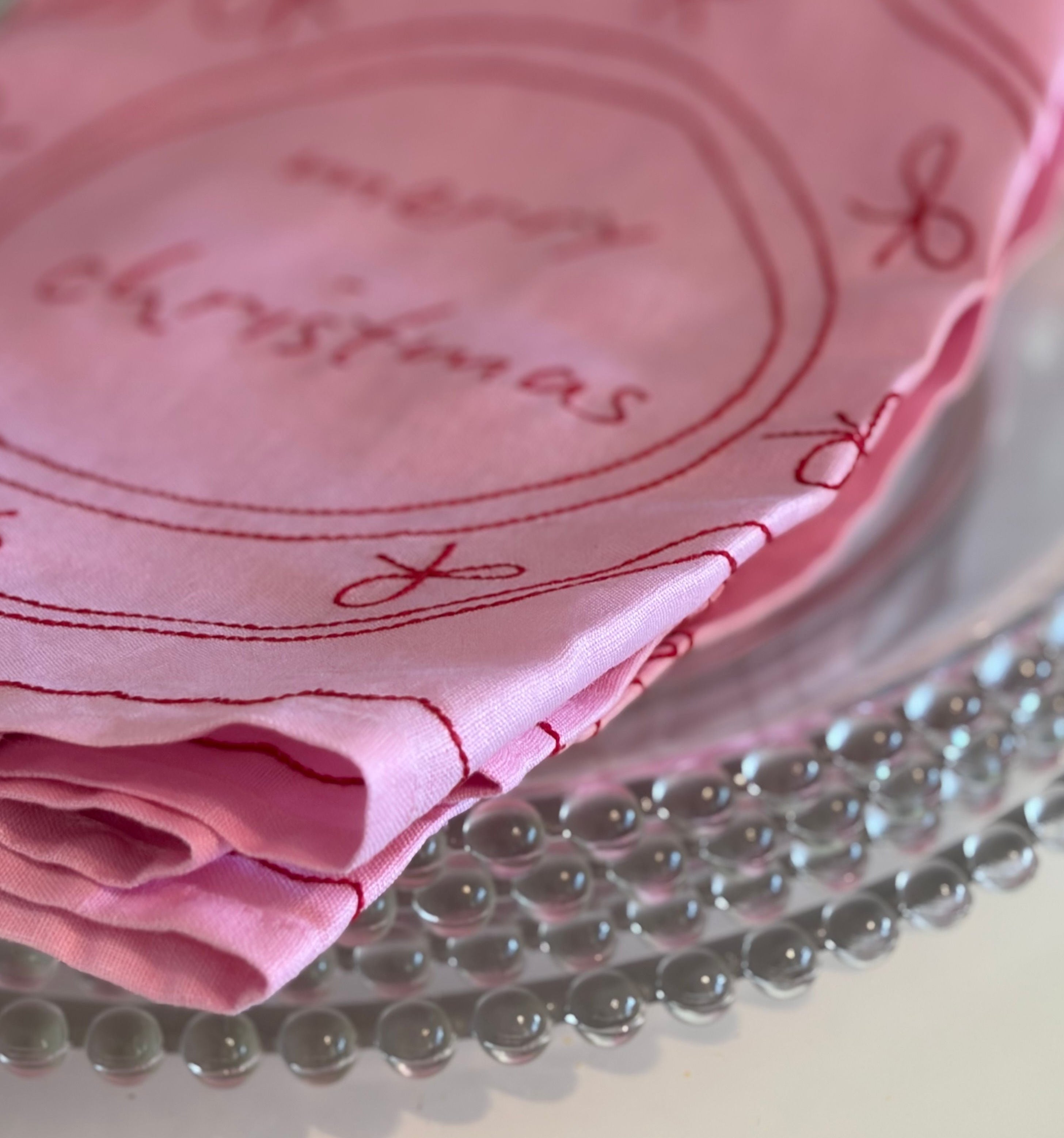 Pink embroidered plate with 'Merry Christmas' on a glass surface
