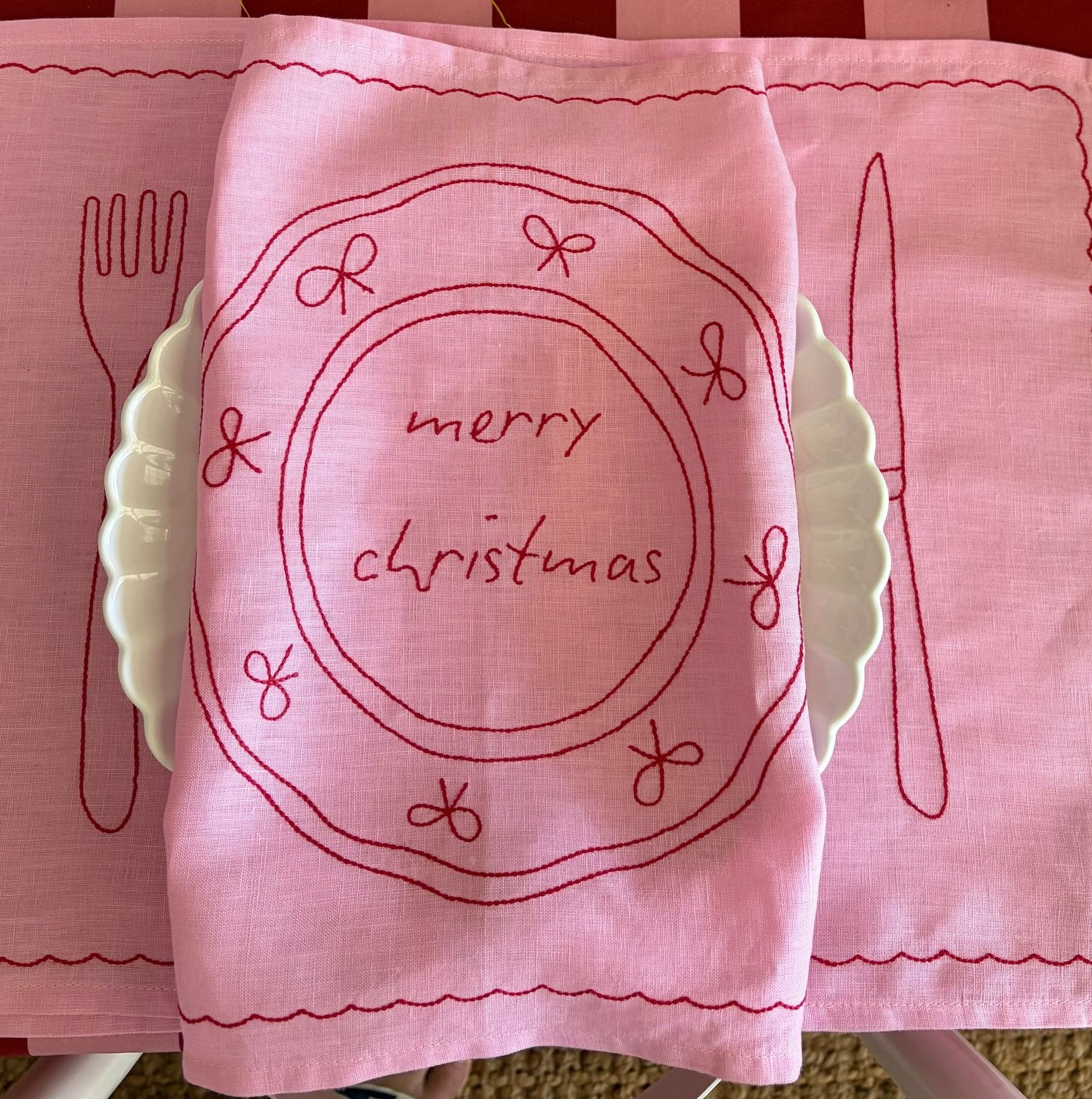 Pink embroidered placemats with 'merry christmas' text on a striped background
