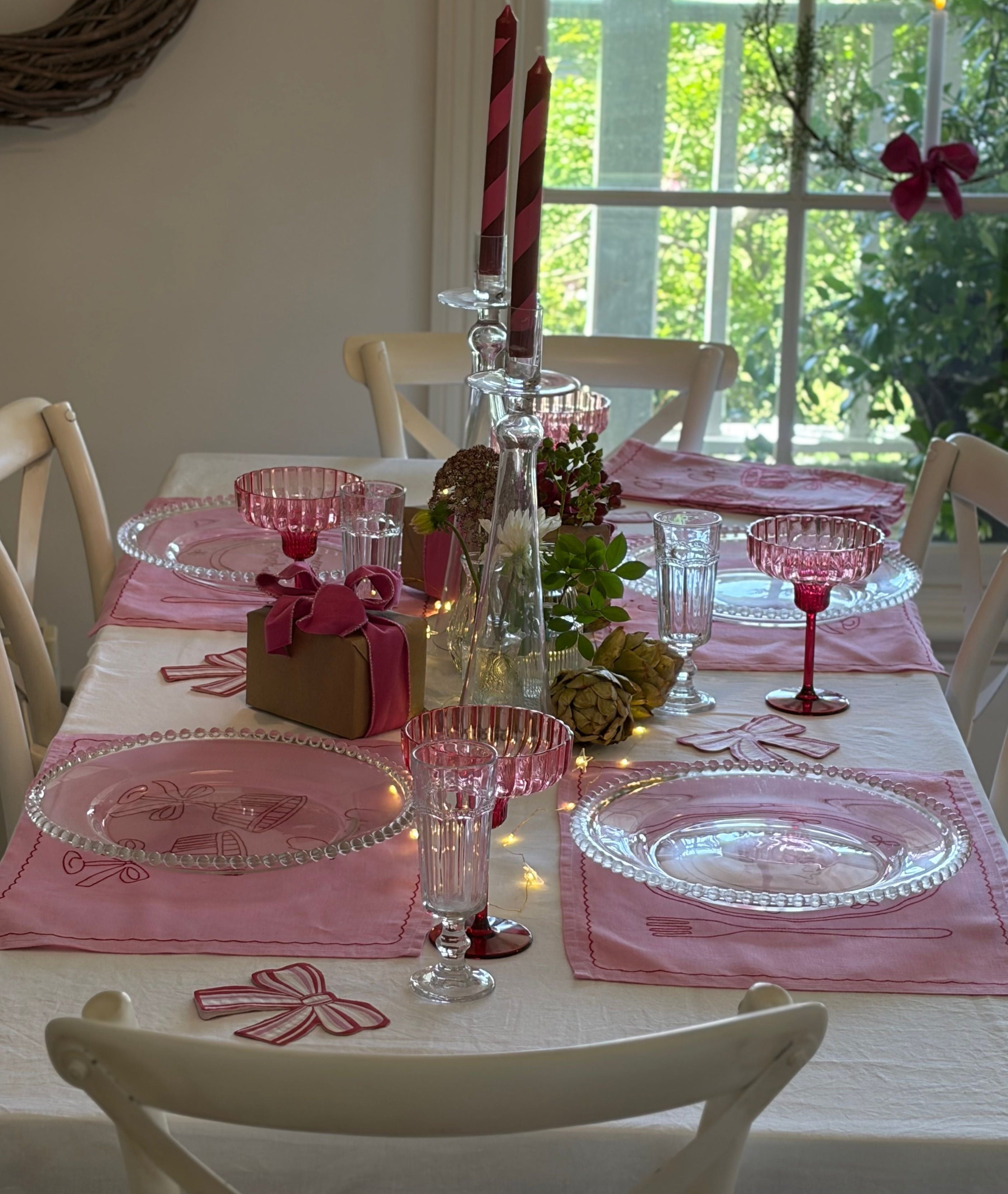 Decorated table with pink placemats, glasses, and candles in a bright room.