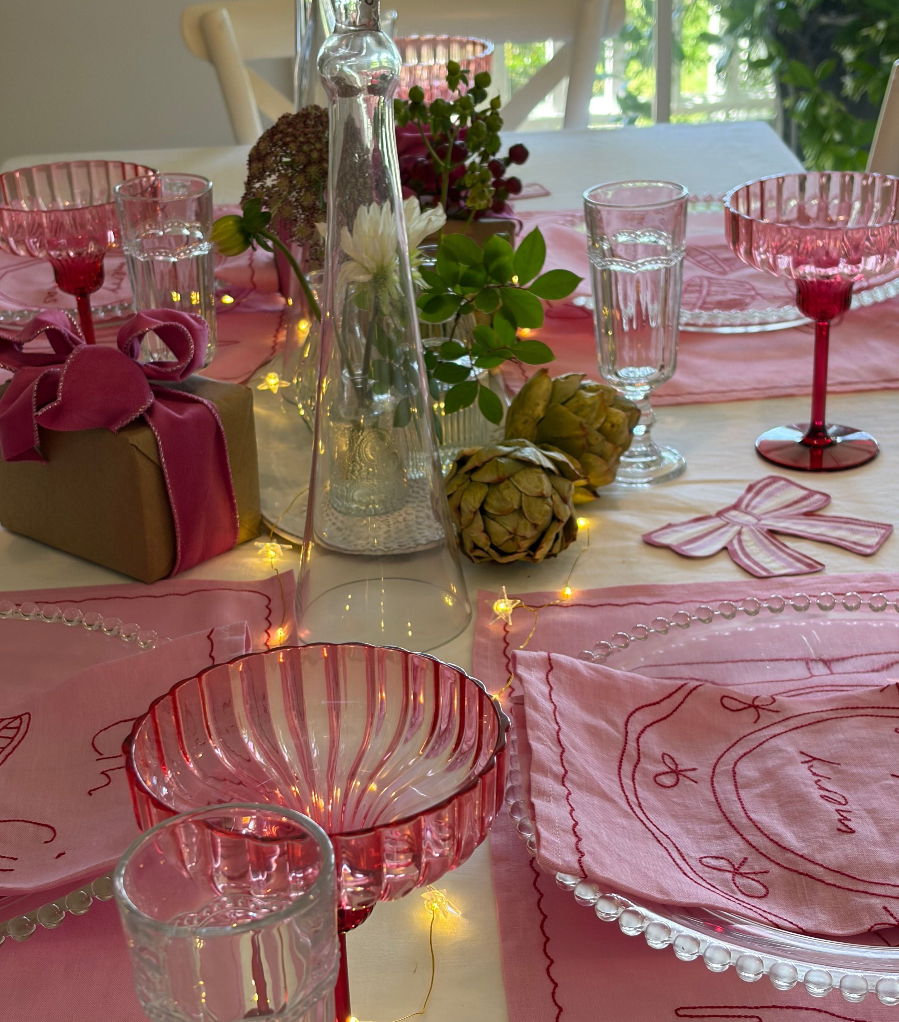 Decorative table setting with pink tablecloths, glasses, and a vase.