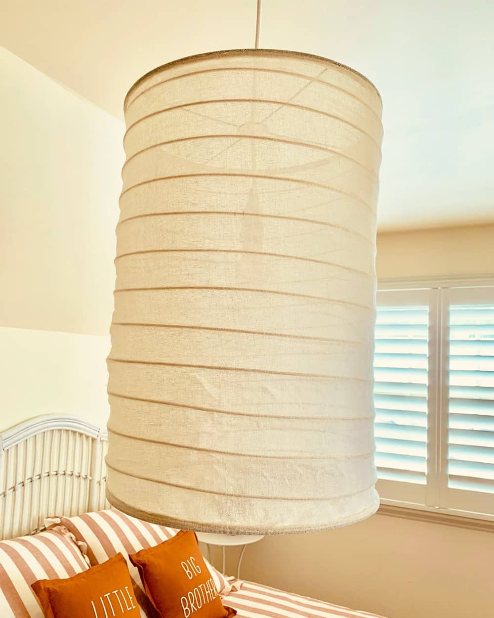 Textured pendant light fixture in a bedroom with striped bedding and 'Little Brother' and 'Big Brother' pillows.