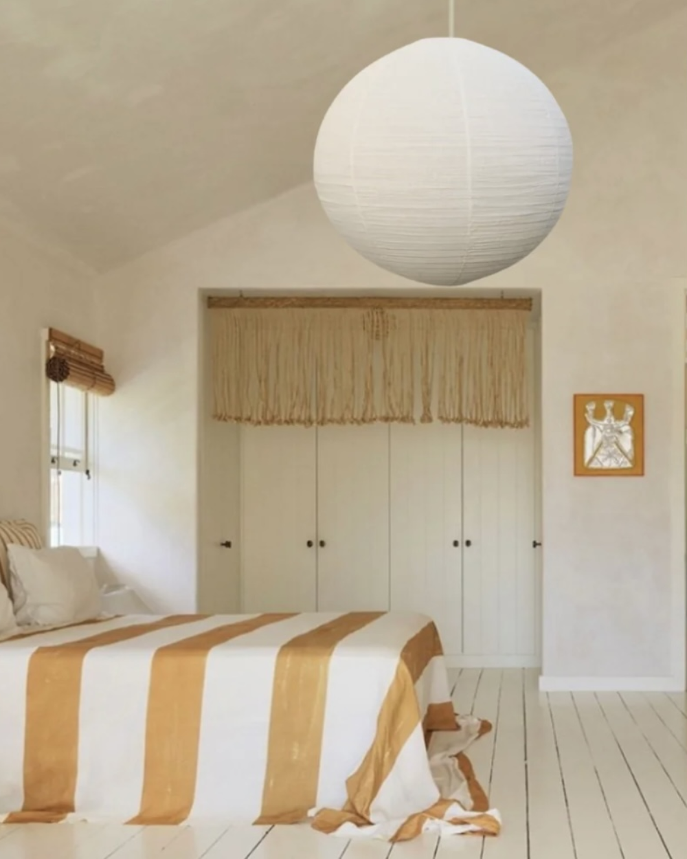 Bedroom with striped bedding, white walls, and a large pendant light.