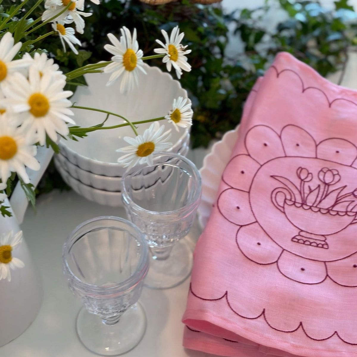 Little Nordic Sol Tulip Plate pink embroidered linen placemat styled with white tableware and fresh daisies.
