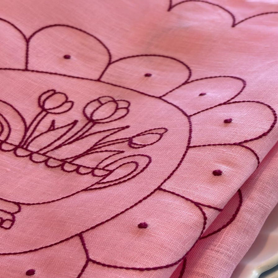 Close-up of Little Nordic Sol Tulip Plate placemat showing raspberry red embroidery on pink linen.