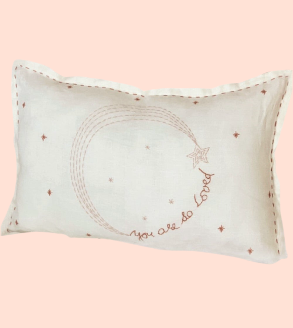 Decorative pillow with embroidered you are loved and star patterns on a pink background